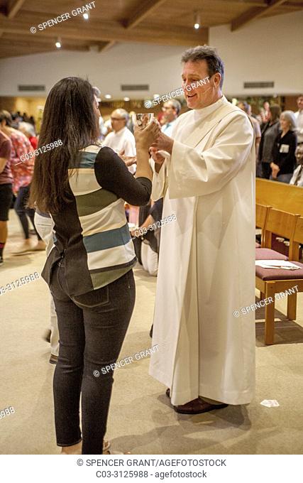 A robed deacon offers the communion cup to a woman parishioner at the conclusion of mass at a Catholic Church in Laguna Niguel, CA