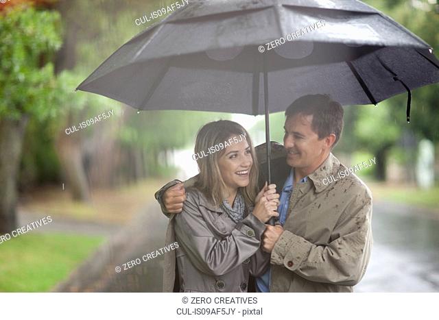 Young woman and mature man walking in rainy park