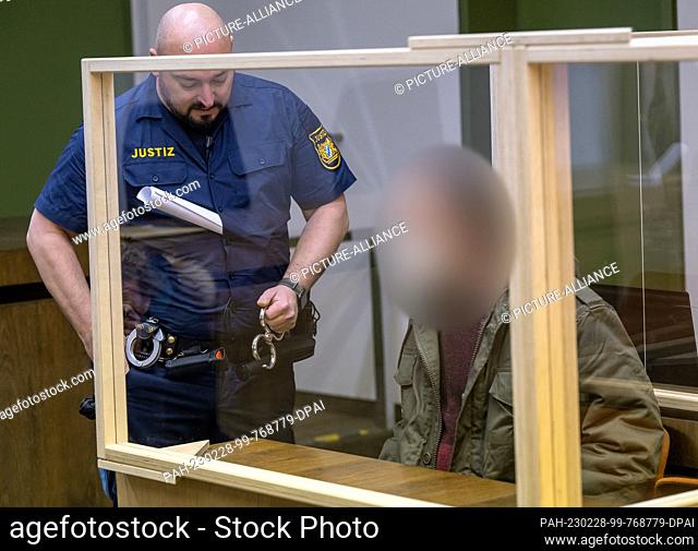 28 February 2023, Bavaria, Munich: The defendant is held in his place in the courtroom by a court official at the start of the trial