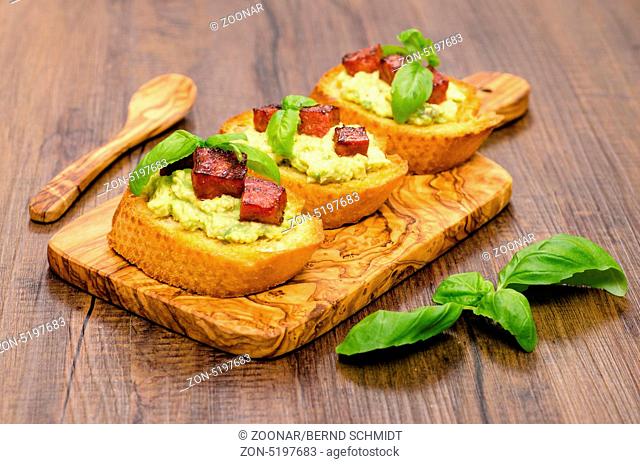 Bruschette mit Avocado-Creme und Chorizo-Wurst auf einem Brett aus Holz