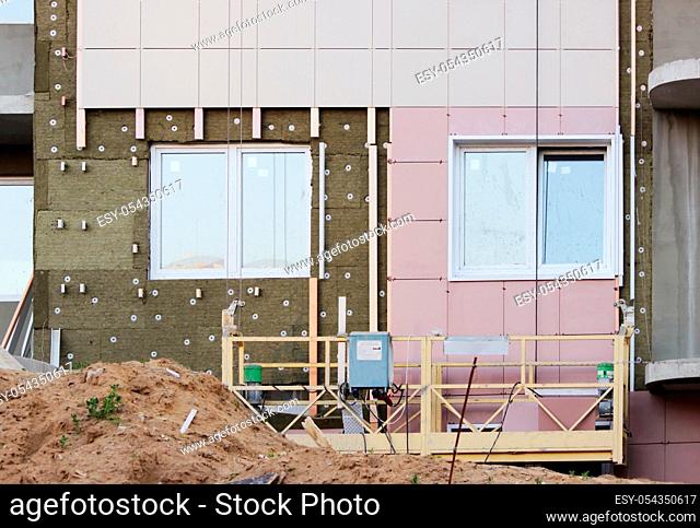 construction suspended yellow cradle without workers on a newly built high-rise building, sand, windows and wall structure with insulated non-combustible...