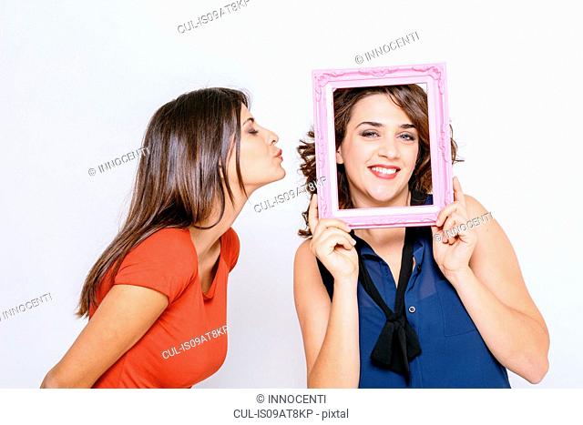 Lesbian couple fooling around with pink picture frame smiling, puckering lips