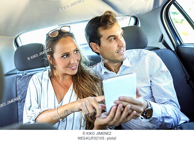 Couple using tablet on back seat of a car