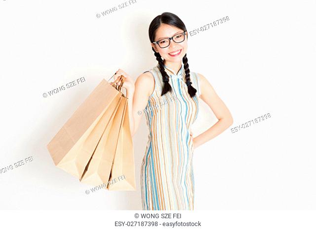 Portrait of young Asian girl in traditional qipao dress shopping, hand holding paper bag, celebrating Chinese Lunar New Year or spring festival