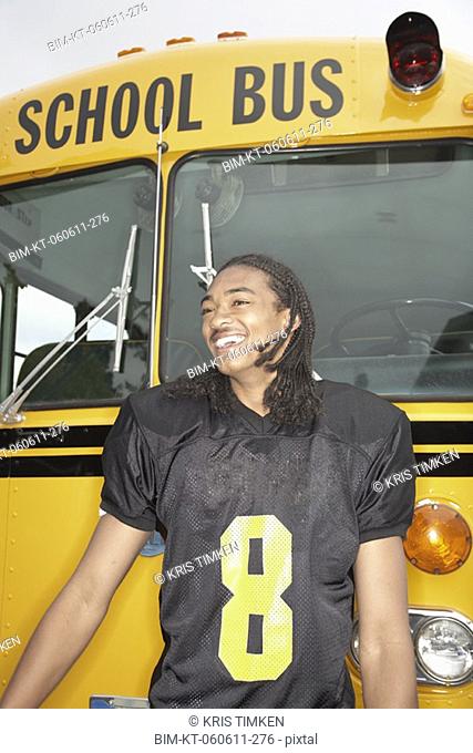 Young African man in football uniform next to school bus