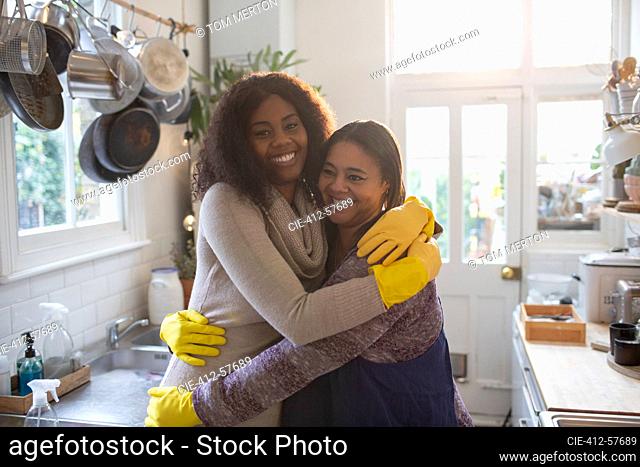 Portrait happy mother and daughter in rubber gloves hugging in kitchen