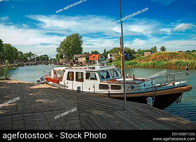 Boat in a pier at the foreground, Vecht River with bridge and brick houses on a sunny day in Weesp. Quiet and pleasant village full of canals and green near...