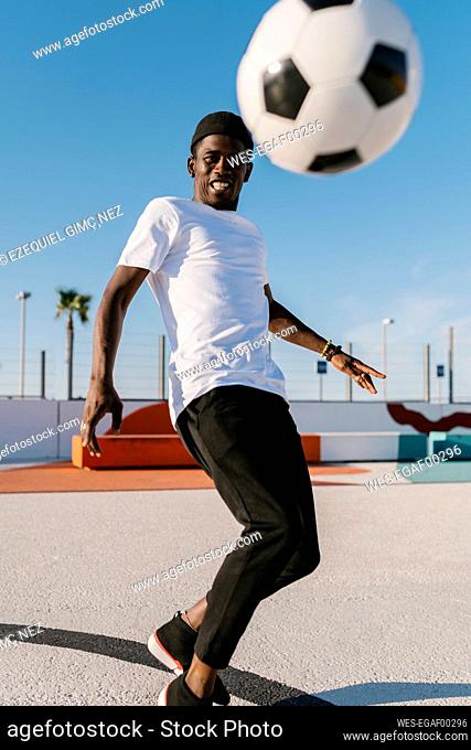 Smiling young man playing soccer against clear sky in court