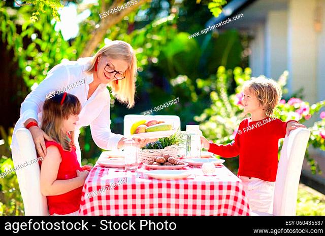 Family eating outdoors. Garden summer fun. Barbecue in sunny backyard. Grandmother and kids eat lunch in outdoor deck. Parents and children enjoy bbq