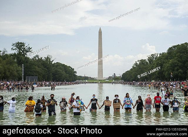 People stand in the cool water of the Reflecting Pool and join hands across the water, during the “Get Your Knee Off Our Necks” March on Washington at the...