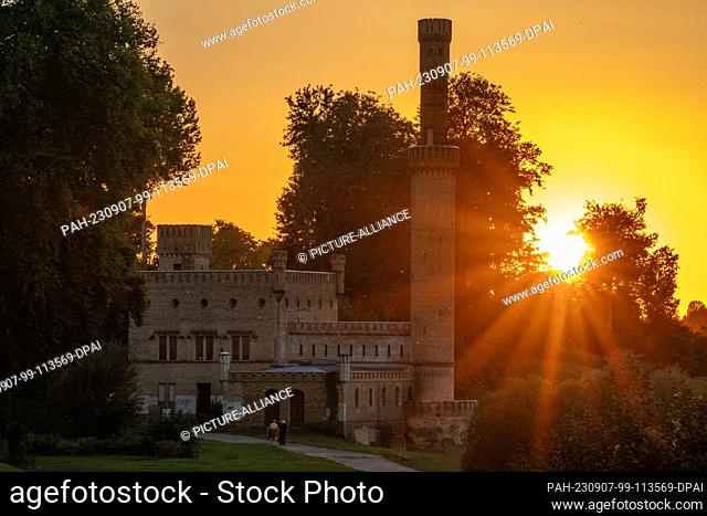 07 September 2023, Brandenburg, Potsdam: Sunbeams shine bright orange behind the steam engine house in Babelsberg Park in Potsdam