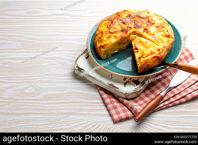 Homemade Spanish tortilla with one slice cut - omelette with potatoes on plate on white wooden rustic background top view