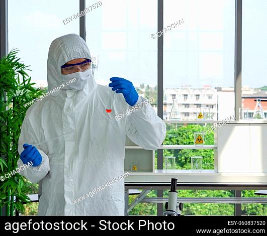 Epidemiological researcher in virus protective clothing use dropper to fill red liquid chemical into test tube. Coronavirus disease 2019 testing process in a...