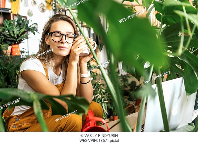 Young woman having a coffee break in a small gardening shop