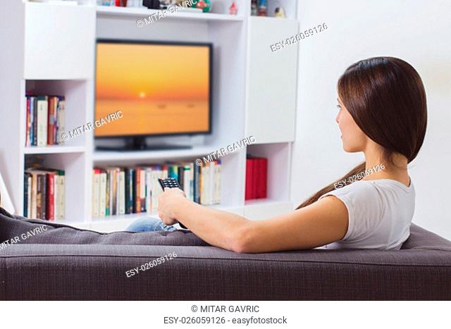 Young woman with remote control, watching TV program at home, Photo on television is from my gallery