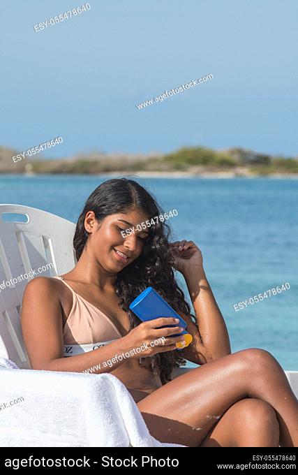 YOUNG WOMAN with sunscreen LOTION AT TROPICAL BEACH on the beach chair