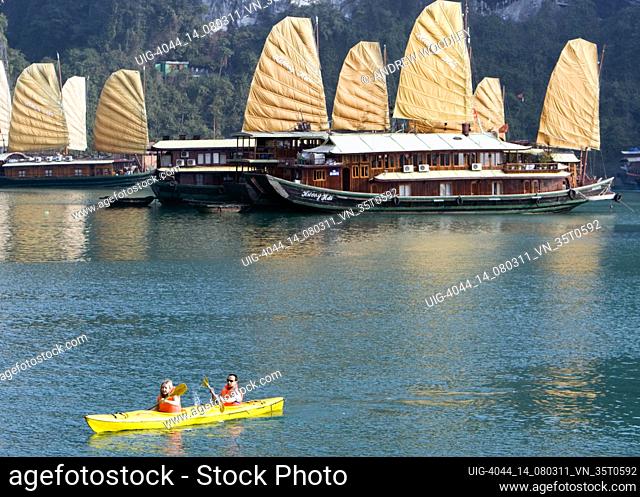 Kayakers paddle past tourist cruising junks Halong Bay Vietnam