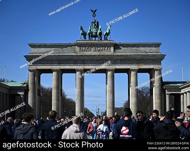 12 April 2023, Berlin: Many tourists come to the Brandenburg Gate in the sunshine and blue sky to take souvenir photos. On the spring-like day