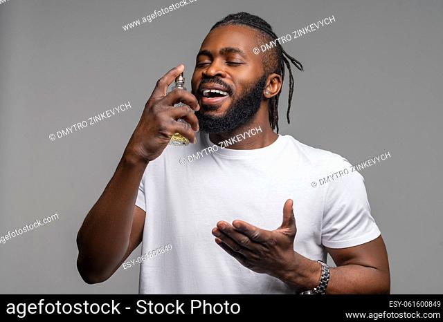 Portrait of a young African American man spritzing himself with perfume and smelling its fragrance