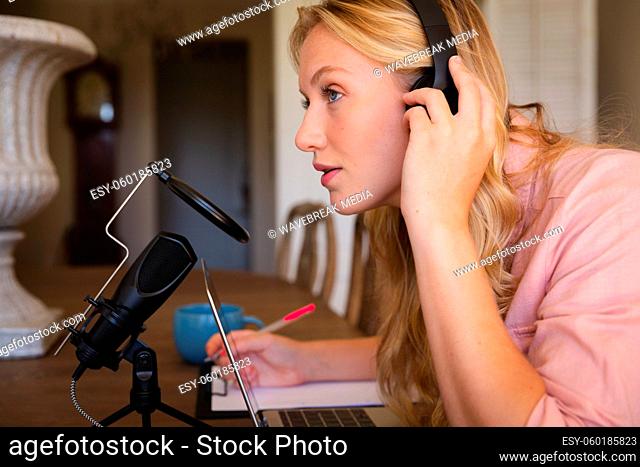 Caucasian woman wearing headphones, using microphone and laptop, listening during podcast