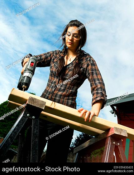 Brunette woman in pigtails drilling 2x4 boards with battery operated drill