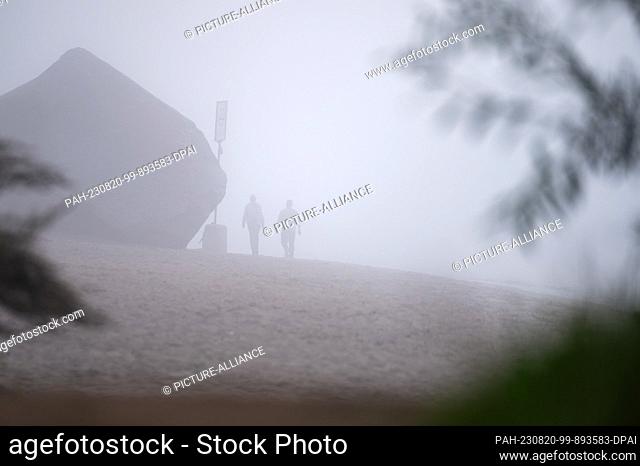 20 August 2023, Hamburg: Walkers walk in the morning in the dense fog next to the old Sweden, a large erratic boulder near Övelgönne