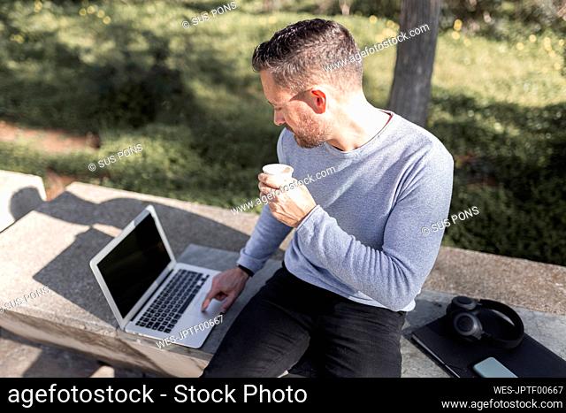 Male entrepreneur with disposable coffee cup using laptop
