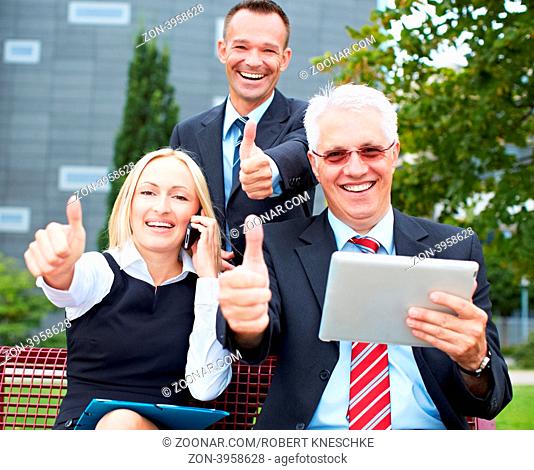 Lachendes Business-Team im Park mit Tablet PC hält ihre Daumen hoch