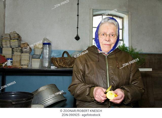 Frau in ihren Siebzigern mit Kopftuch sitzt in der Waschküche und schält sich einen Apfel
