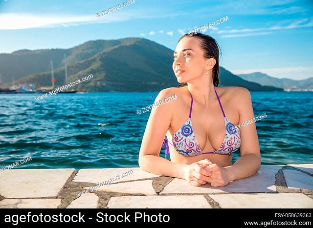 Lovely brunette posing in summer in the water, dressed in a swimsuit on a background of mountains and sea