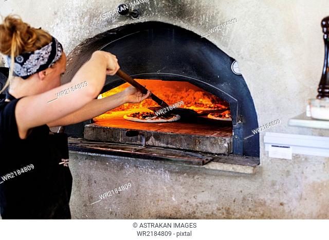 Side view of woman positioning pizza in oven with spatula at restaurant