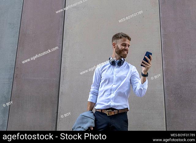 Smiling businessman using mobile phone while standing against wall