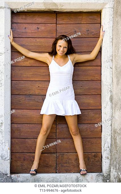 Attractive young woman in White short dress is standing on porch with spread hands and legs