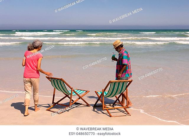 Senior couple with sun lounger standing on beach