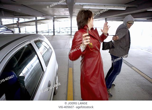 A man is sneaking up to a woman and snatches away her handbag in a parking garage. - LEIPZIG, GERMANY, 01/03/2007
