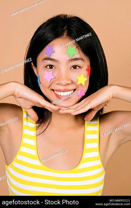 Smiling woman with multi colored star stickers against brown background