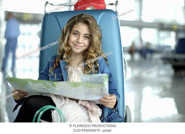 Young girl in airport with map and luggage