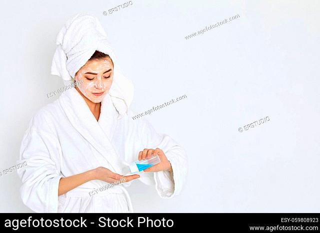 woman in white bathrobe with towels on head holds cotton swab and tonic. Skin cleansing. copy space
