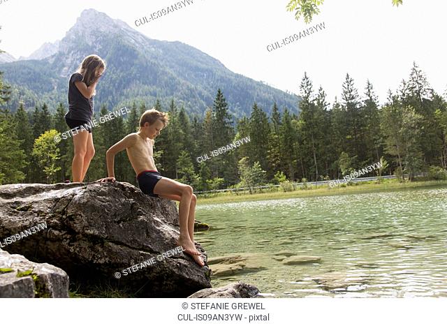 Brother and sister on lake boulder, Hintersee, Zauberwald, Bavaria, Germany