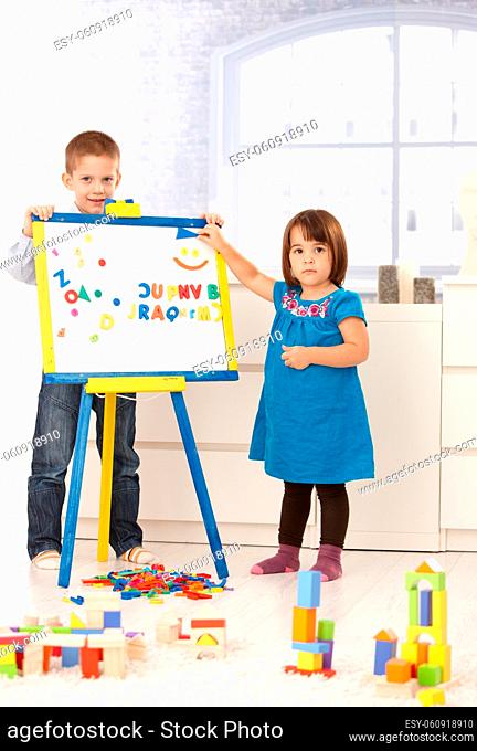 Portrait of creative small kids standing at drawing board, playing with alphabet