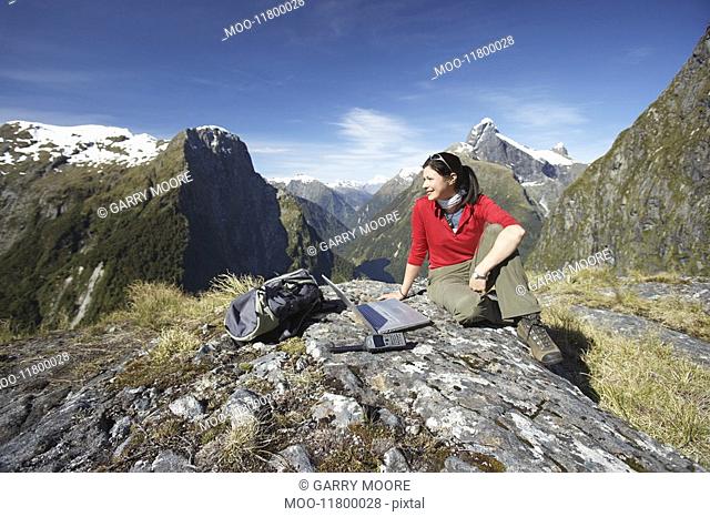 Woman sitting with laptop on mountain peak