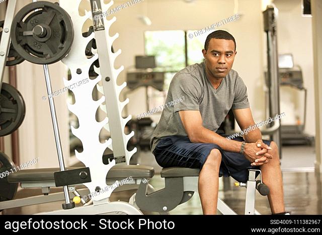 African American man resting in health club on weight-lifting bench