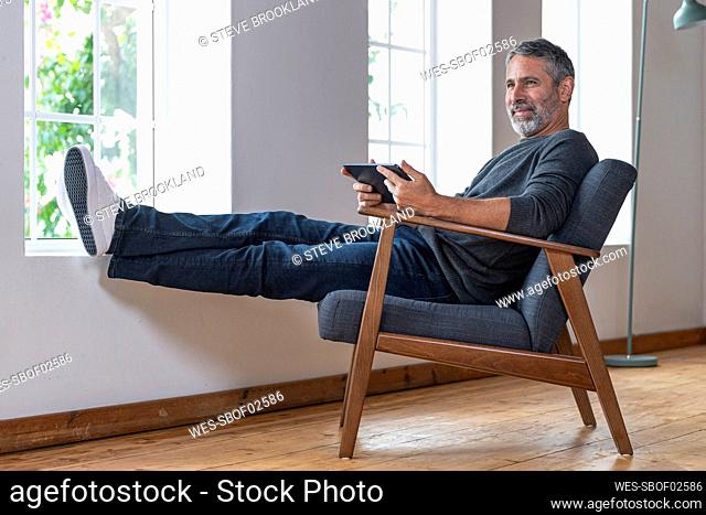 Smiling businessman using digital tablet while sitting on armchair at home
