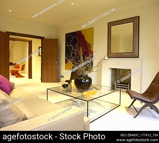 Sitting room with open double doors, seating area with glass box coffee table, and a large mirror over the fireplace
