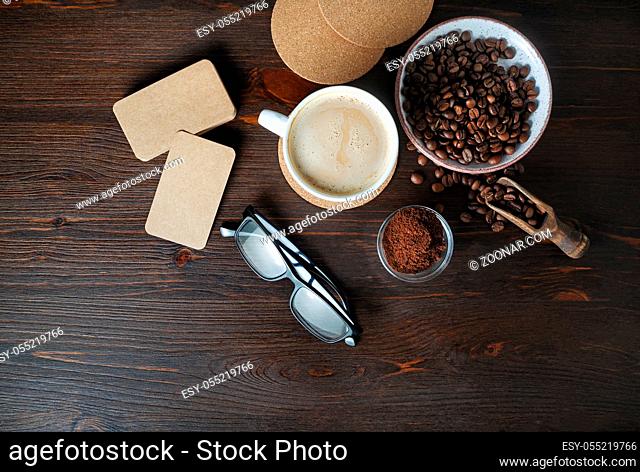Coffee cup, kraft business cards, roasted coffee beans, glasses and coffee ground on wood table background. Flat lay