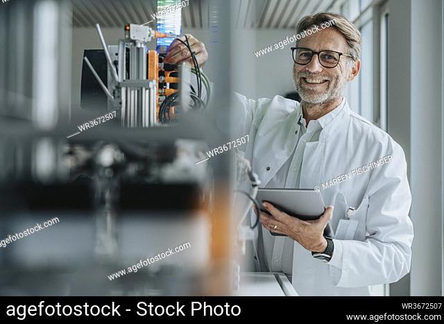 Smiling mature man with digital tablet inventing machinery in laboratory