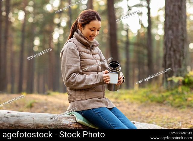 asian woman with thermos drinking tea in forest