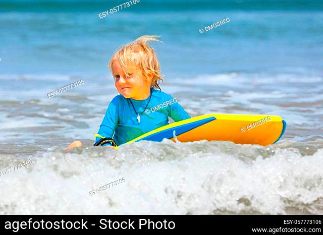 Happy baby boy - young surfer ride on surfboard with fun on sea waves. Active family lifestyle, kids outdoor water sport lessons and swimming activity in surf...