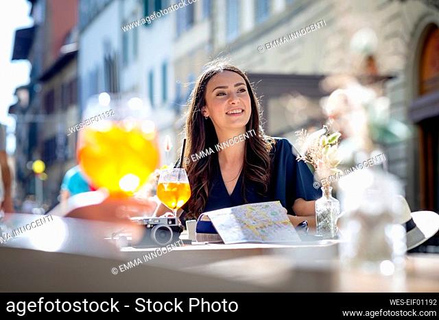 Female tourist smiling while looking away at sidewalk cafe on sunny day