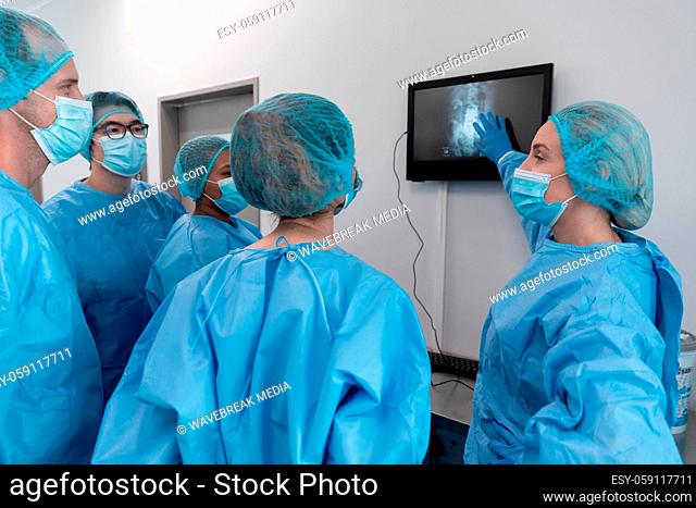 Diverse group of male and female surgeons in operating theatre wearing face masks looking at screen